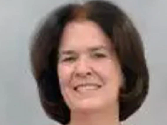 Smiling woman with short dark brown hair, wearing a red buttoned sweater, standing in front of a gray background.