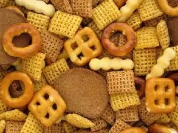 Close-up image of a snack mix containing pretzels, cereal squares, and crackers in various shapes and textures.